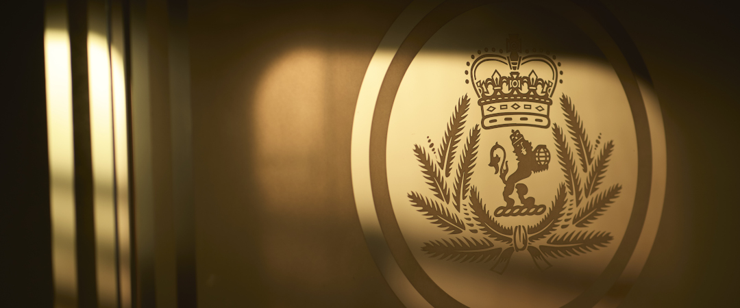 Goldenes, im warmen Licht schimmerndes Logo der Reederei Cunard mit Krone, Löwe und Lorbeerkranz auf metallischer Oberﬂäche.